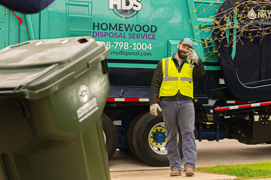 garbage truck driver smiling and waving at a customer with a cart