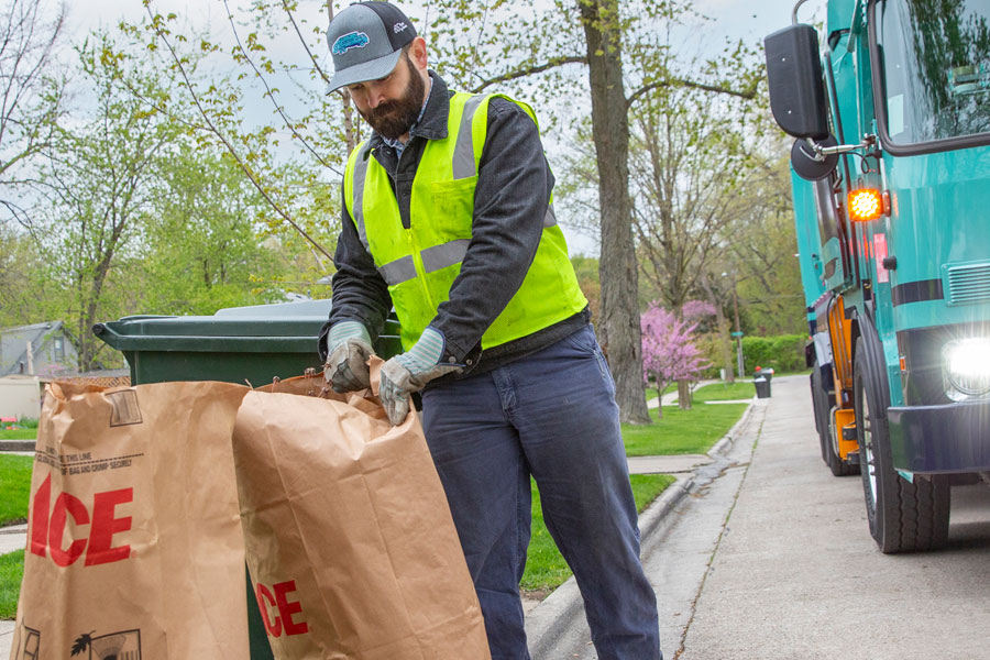 worker collecting yard waste in bags at the curb